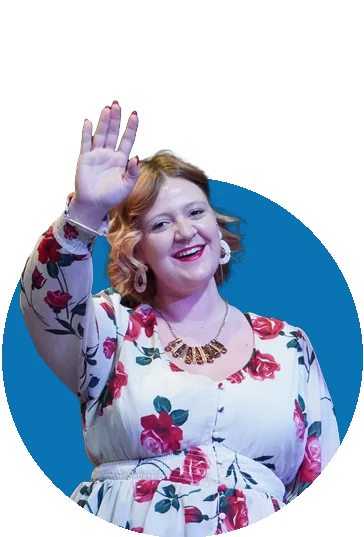 A smiling Tapestry actor in a rose-print blouse waves on stage in The 25th Annual Putnam County Spelling Bee