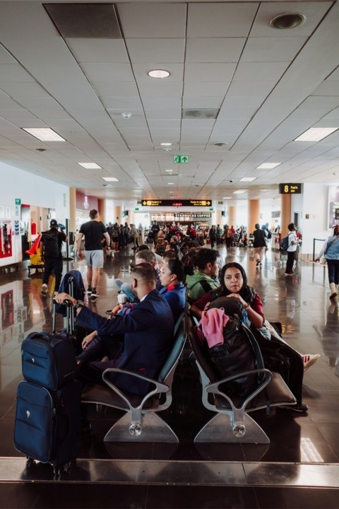 Travelers seated in airport lounge area with luggage, waiting at a busy terminal gate.