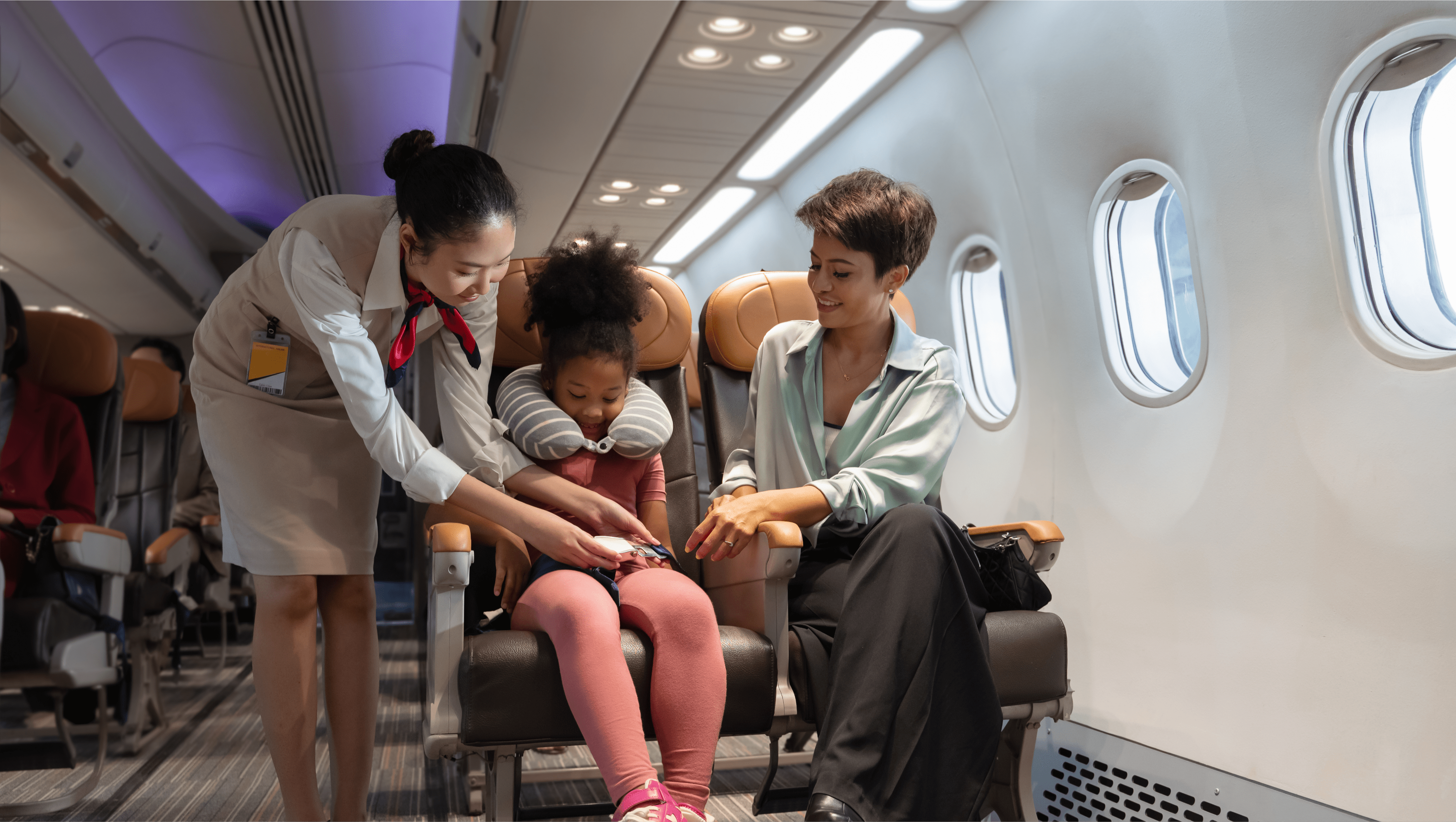 Flight attendant helping child fasten seatbelt beside mother during airplane flight.