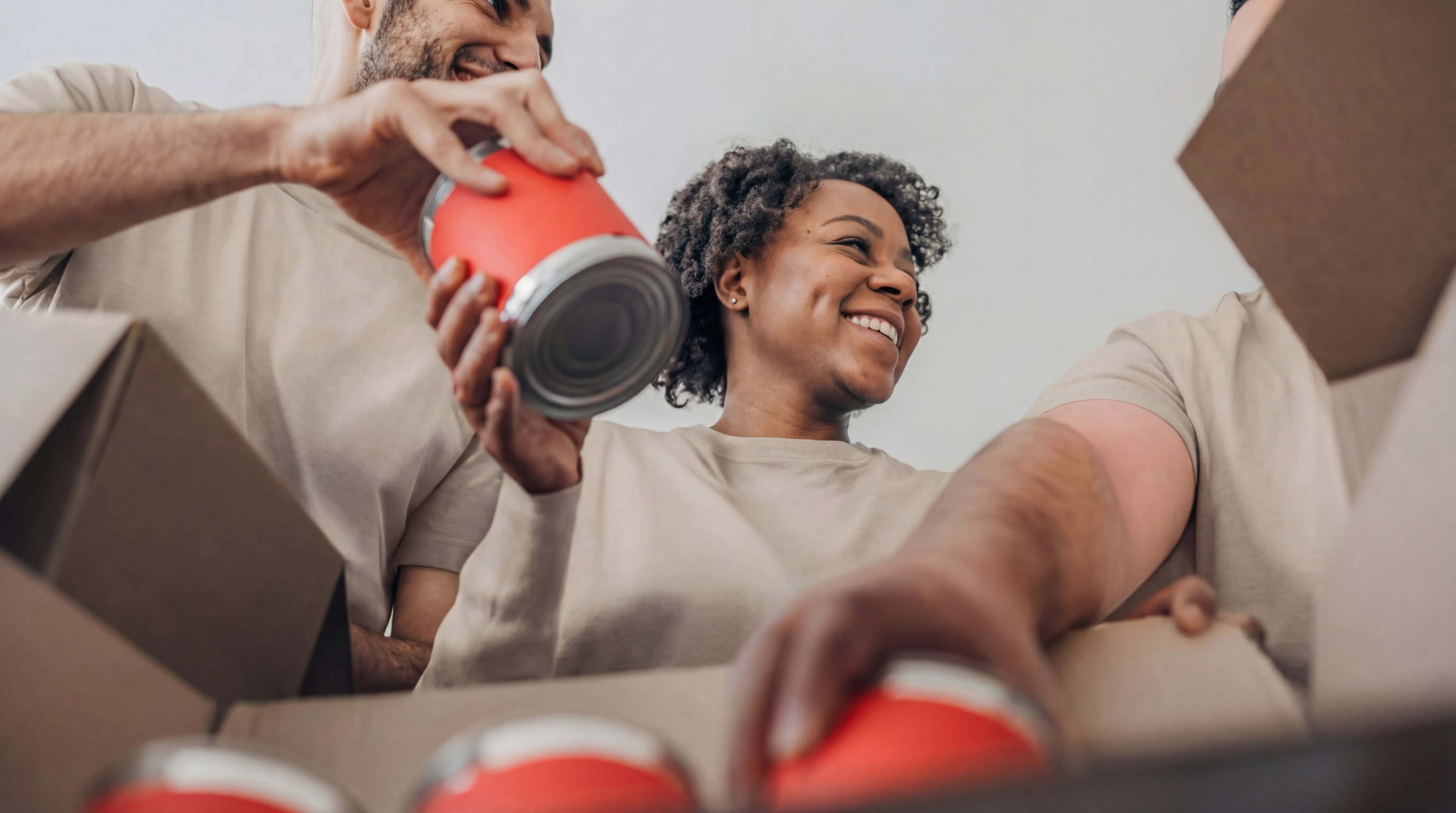 Smiling diverse volunteers packing cans into a cardboard box.