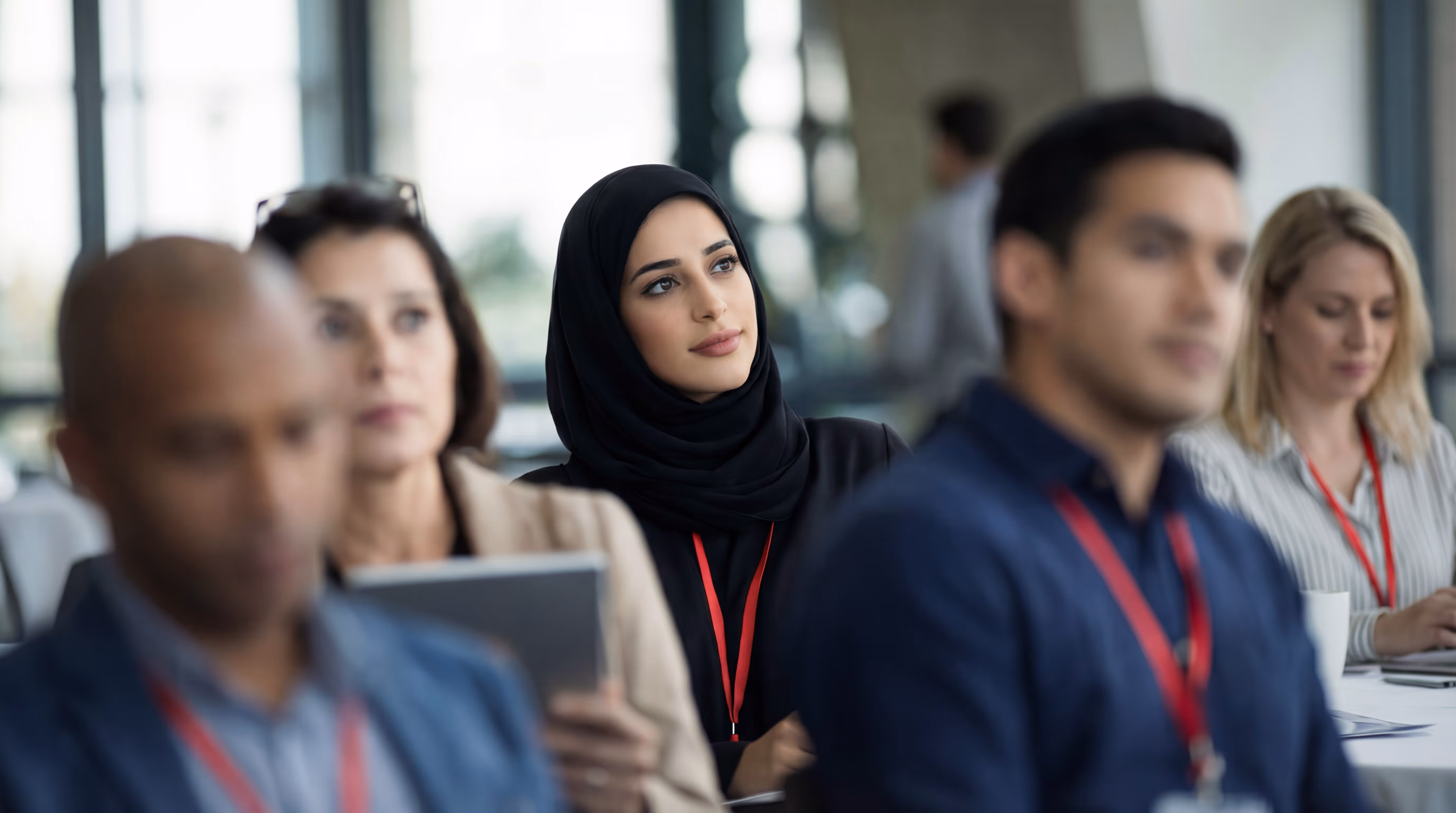 Diverse group of adults attending a conference or seminar, with a woman in a black hijab in focus.