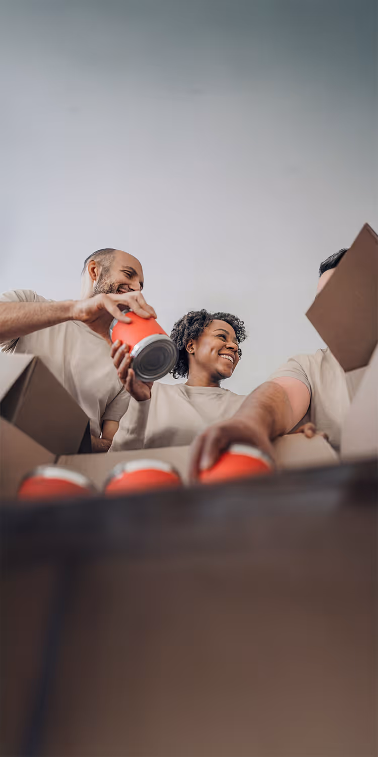 Three diverse volunteers smiling and packing canned food into boxes.