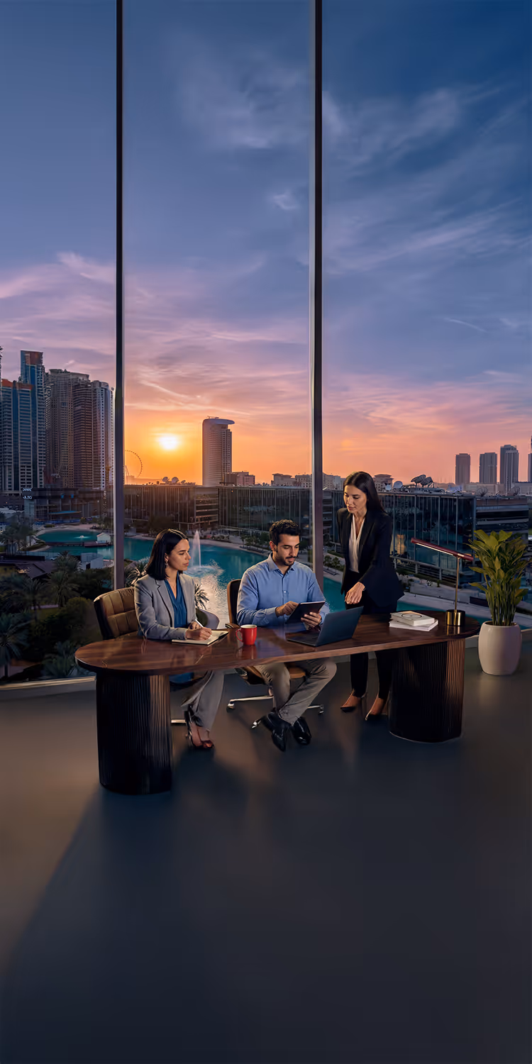 Three business professionals collaborating in an office with a large window overlooking a cityscape at sunset.