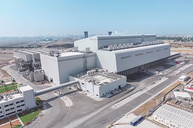 A large industrial facility with multiple connected white buildings and surrounding roads under a clear blue sky.