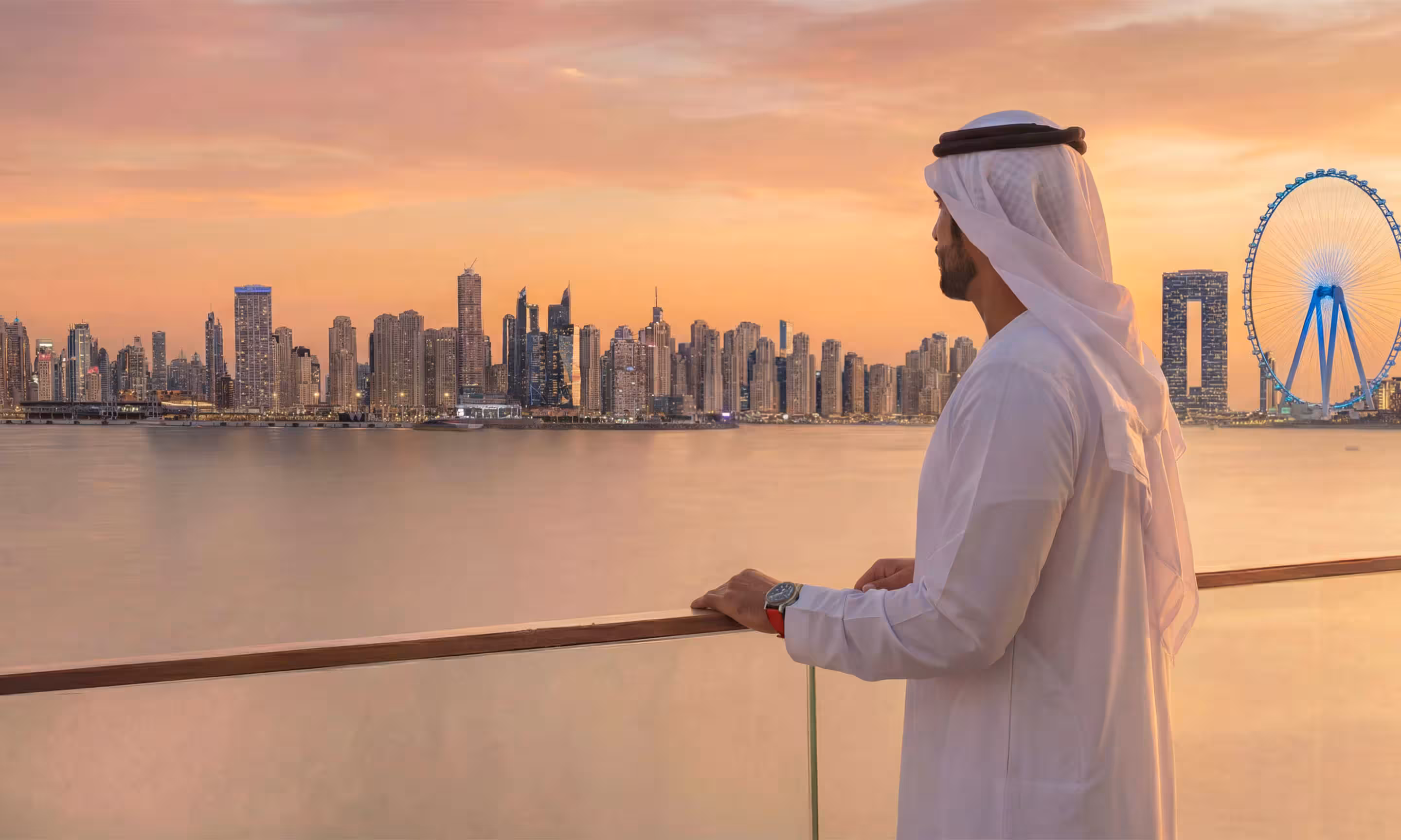 Man in traditional Middle Eastern attire looking at a city skyline at sunset with a large Ferris wheel in the background.