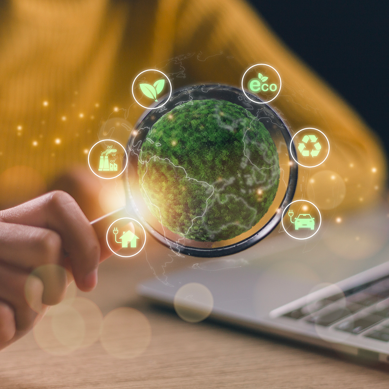 Hand holding magnifying glass over a green planet with eco-friendly icons floating around it.