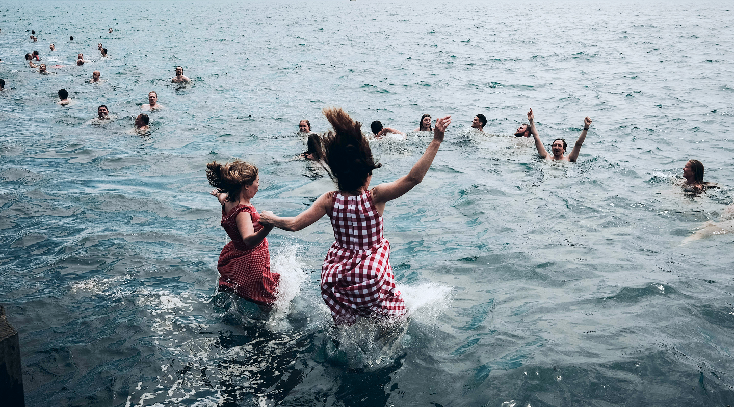 Menschen springen gemeinsam ins Wasser und schwimmen beim Neujahrsschwimmen des Rotary Clubs im Auesee in Wesel