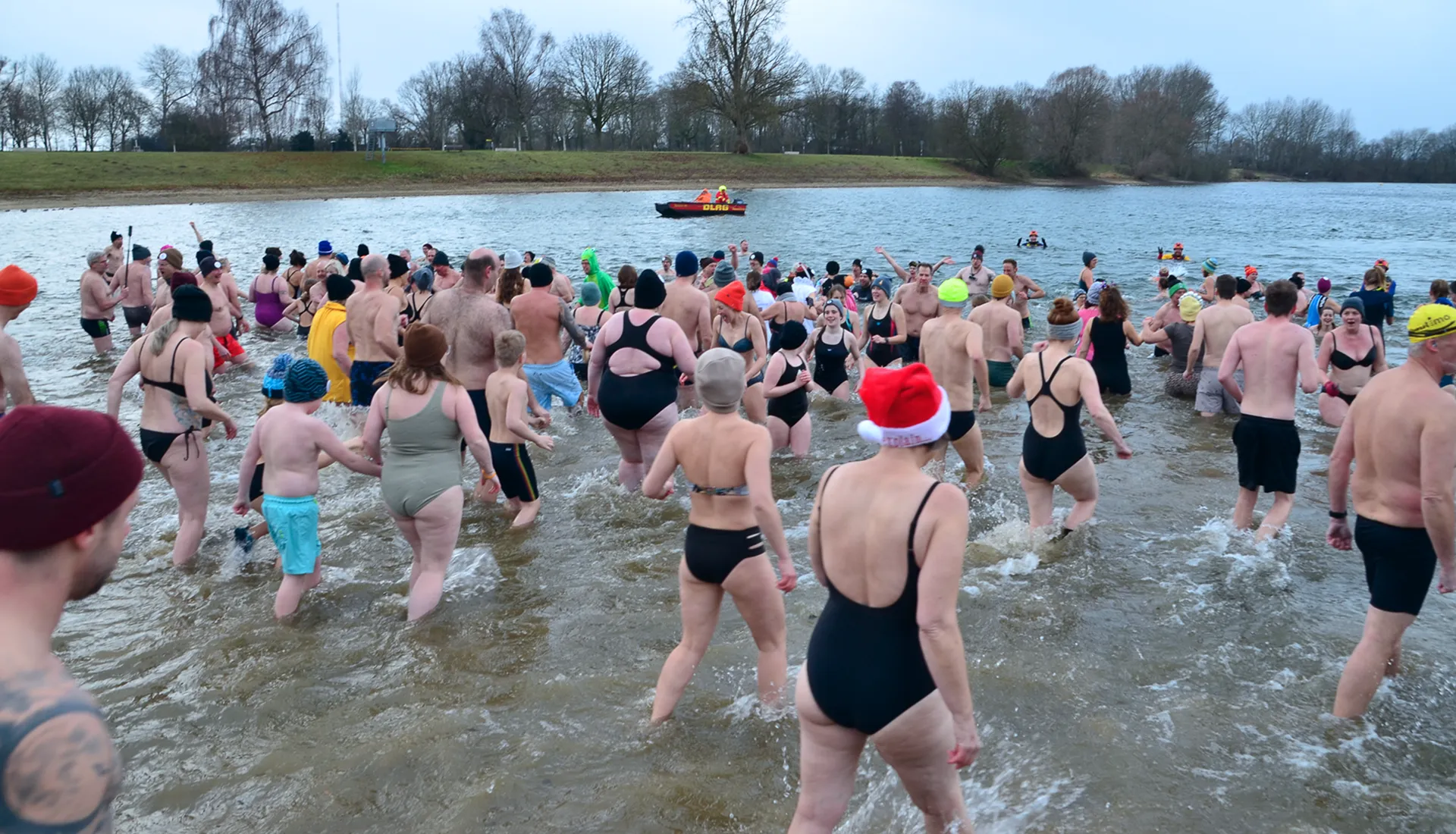 Eine große Gruppe von Menschen in Badekleidung steigt in einen See; einige lächeln und planschen.