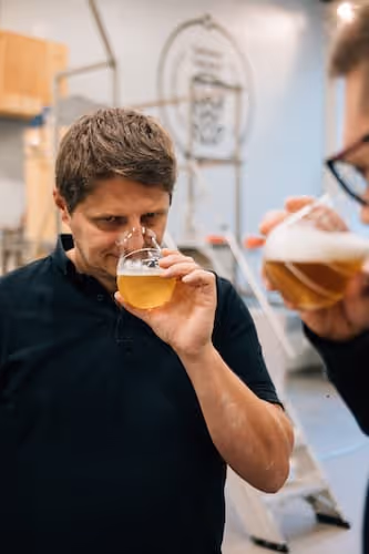 Zwei Männer riechen an Gläsern mit hellem Bier in einer Brauerei.