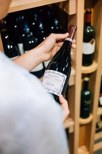 Person hält eine Weinflasche vor einem Weinschrank mit mehreren Flaschen.