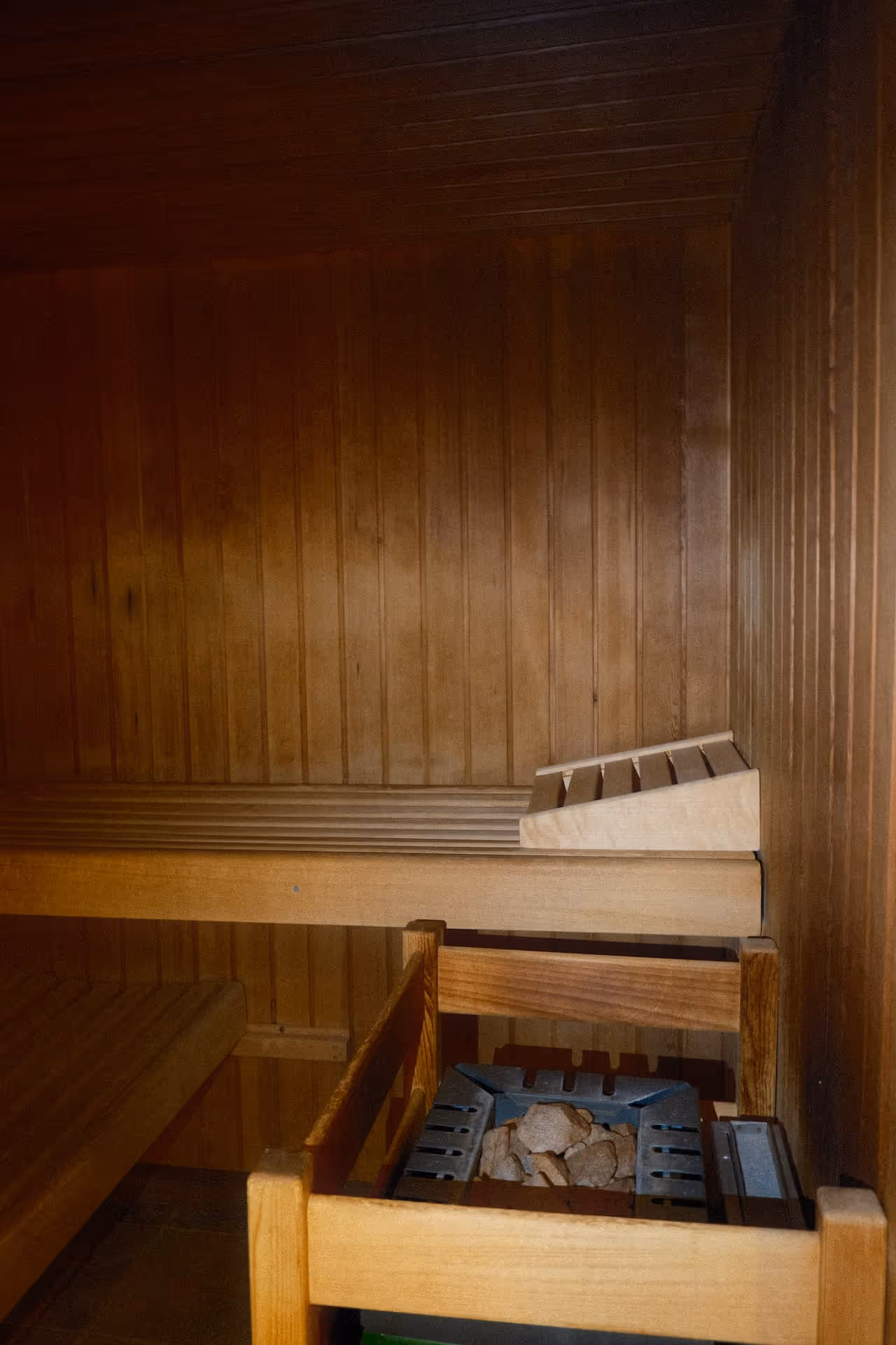 Innenansicht einer finnischen Sauna mit Holzbänken und einem beheizten Saunaofen mit Steinen.