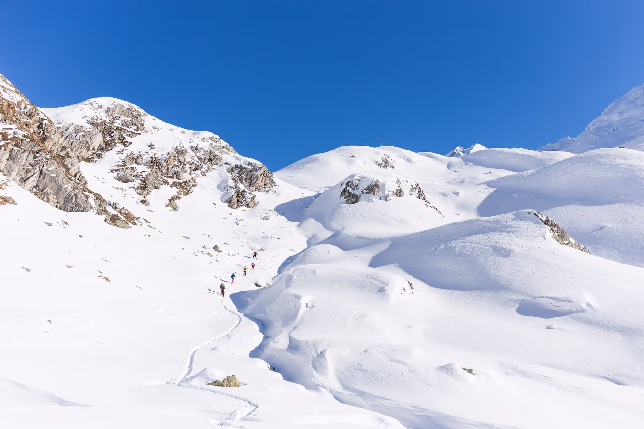 Eine Gruppe von Skitourengehern steigt eine verschneite Berglandschaft mit klarem blauem Himmel empor.