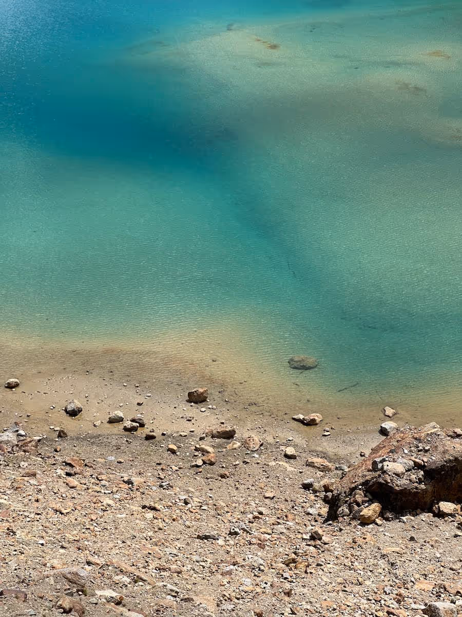 Ufer mit Steinen am Rand eines klaren, türkisfarbenen Sees.