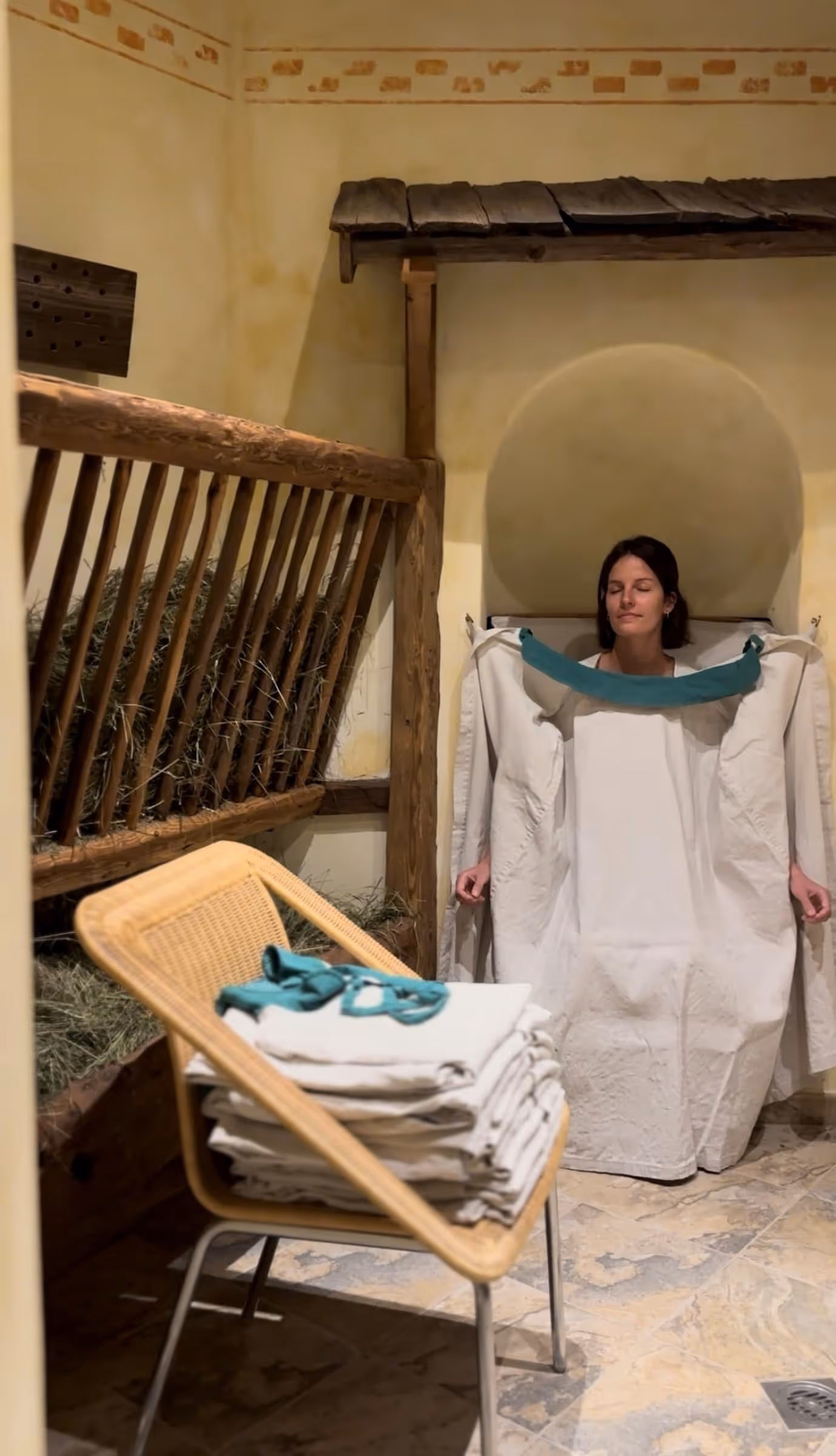 Frau sitzt entspannt in einem traditionellen Kurhaus und trägt eine große weiße Umhüllung mit grünen Griffen.