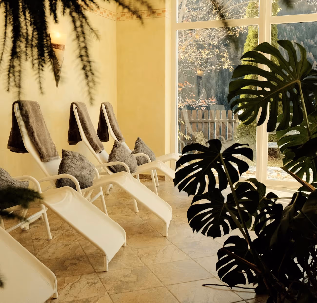 Helle Saunaliege mit grauen Handtüchern und Kissen neben großen Fenstern mit Außenausblick.