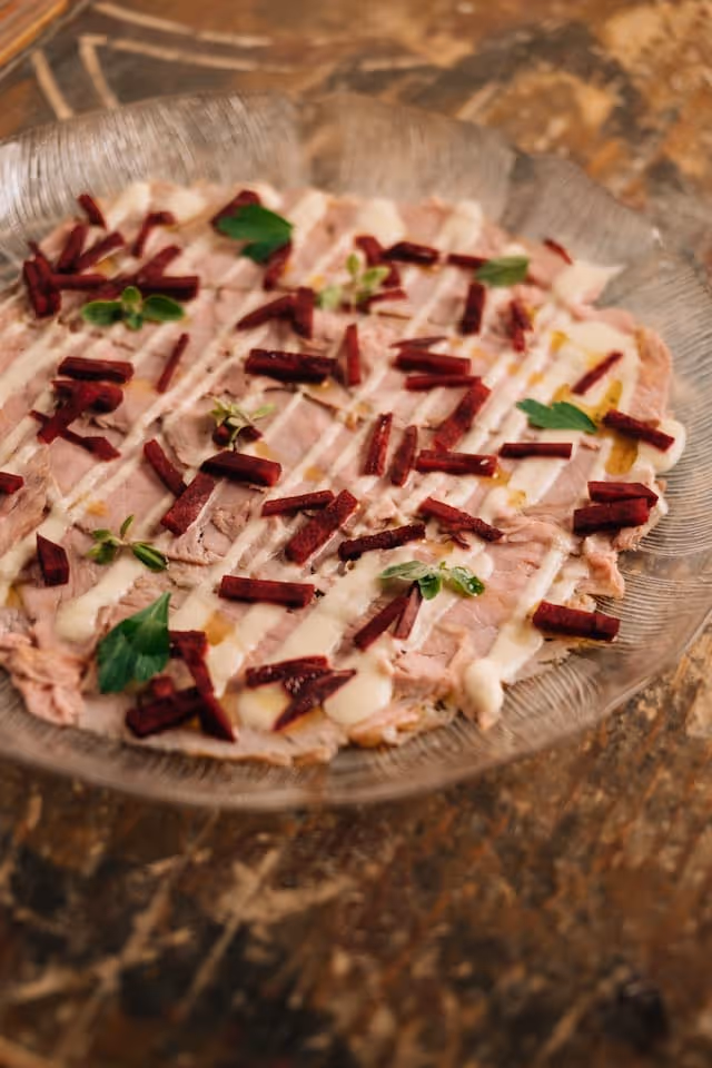 Auf einem gläsernen Teller angerichtete dünn geschnittene Tafelspitzscheiben, garniert mit roten Rübchenstreifen und grünen Kräutern.