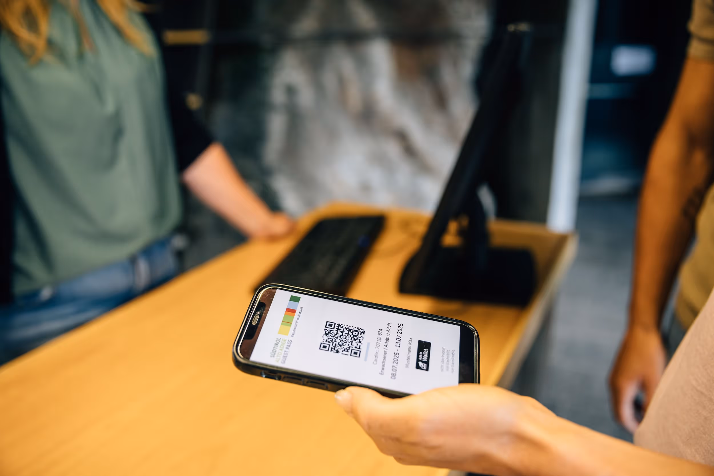 Person hält ein Smartphone mit einem digitalen Ticket und QR-Code über einen Verkaufstresen.