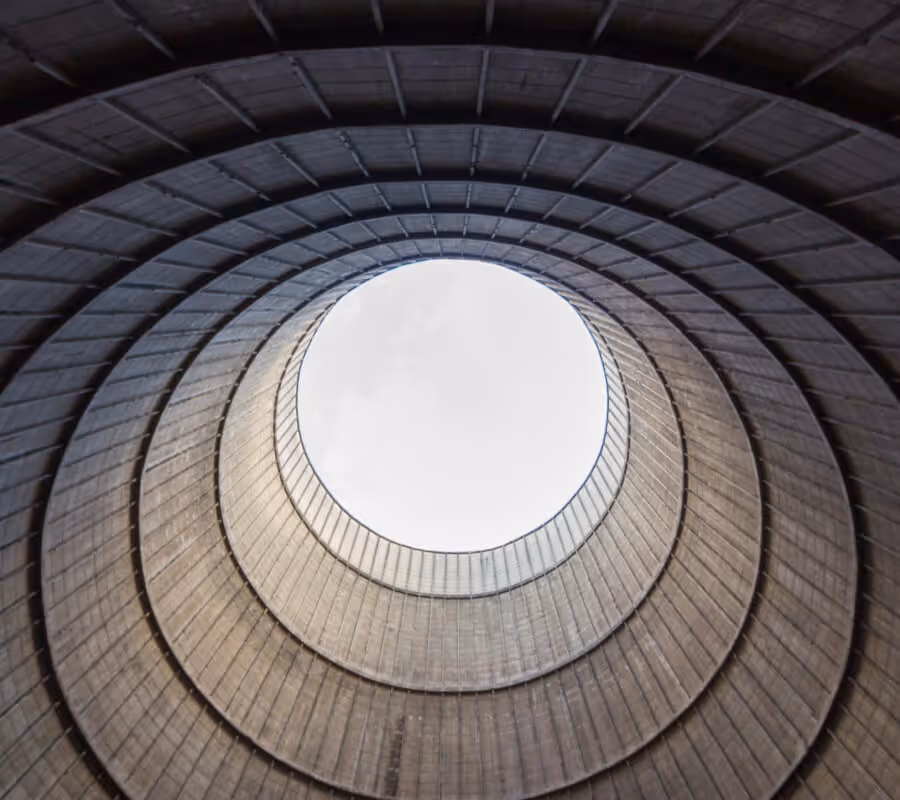 View looking up into the circular opening of a large industrial cooling tower with concentric concrete rings.