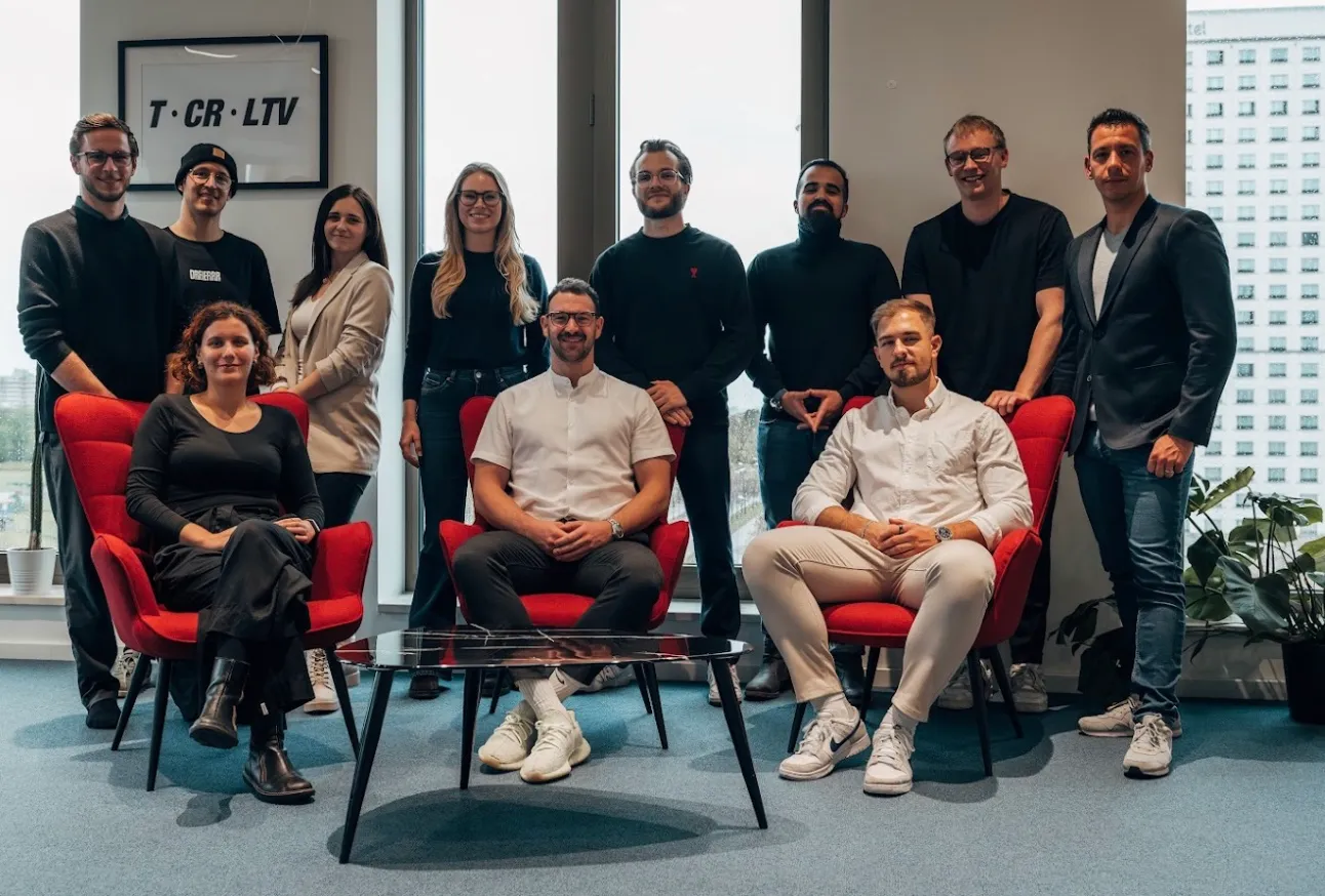 Team of professionals posing together in a modern office with large windows and red chairs, representing the collaborative spirit and expertise driving IT and AI (KI) education for digital commerce