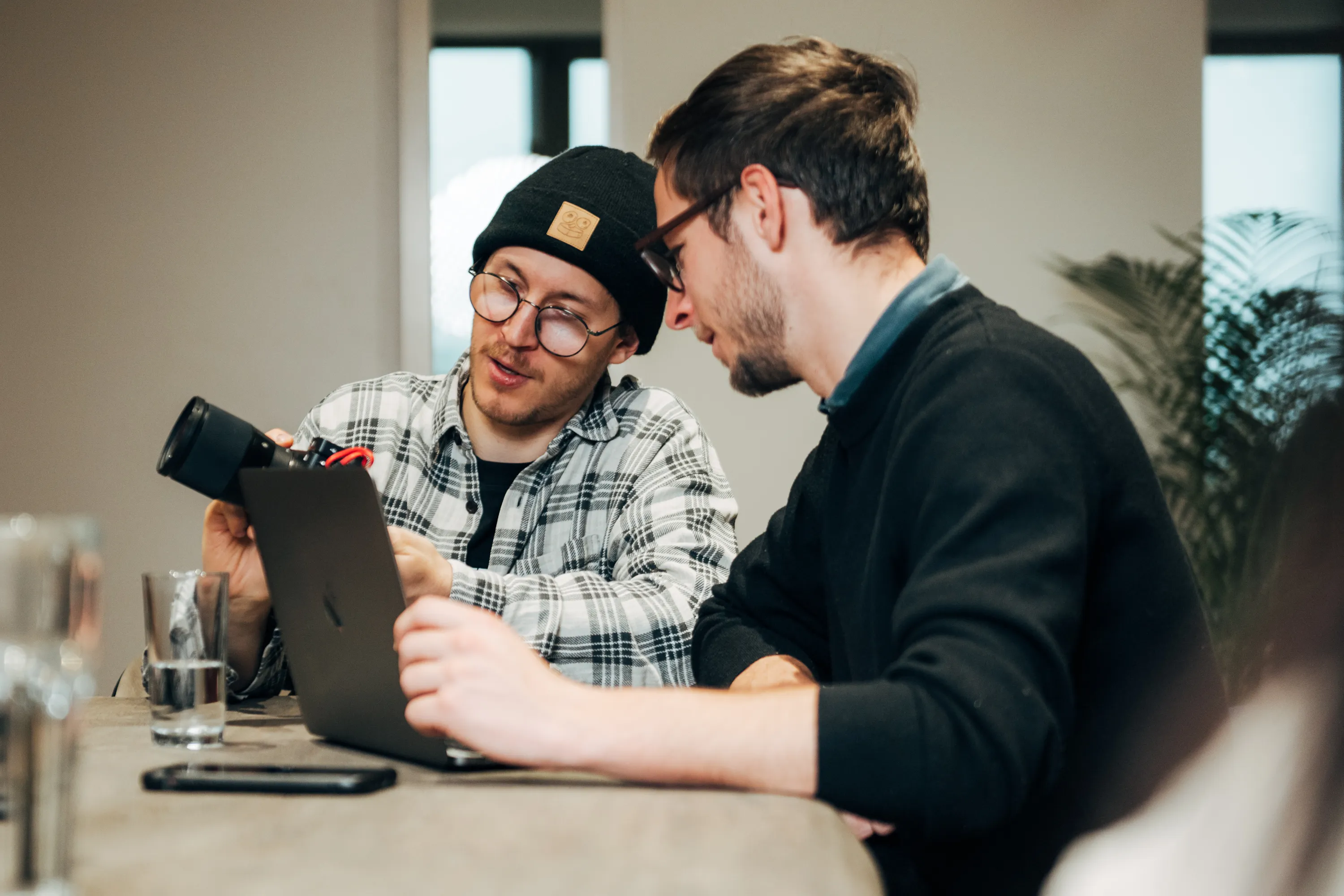 Two men reviewing camera equipment together while working on a laptop, illustrating hands-on, tech-driven learning in IT and AI (KI) training for digital commerce