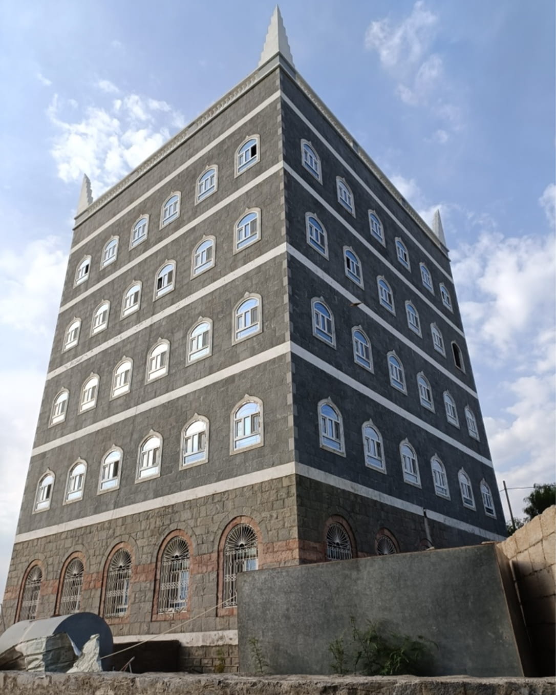 مبنى يافعي حجري طويل مستطيل الشكل به نوافذ upvc مقوسة متعددة وزخارف بيضاء تحت سماء غائمة جزئيًا.