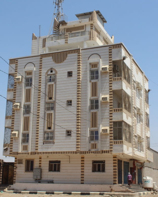 مبنى سكني مكون من أربعة طوابق باللونين البيج والبني مع نوافذ upvc وشرفات متعددة تحت سماء زرقاء صافية.