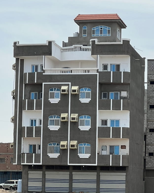 مبنى سكني متعدد الطوابق بواجهة رمادية داكنة وبيضاء وشرفات متعددة ووحدات تكييف هواء و نوافذ upvc