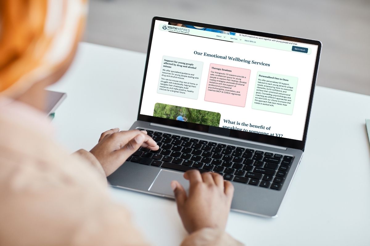 Close-up of a laptop screen showing the Youth Inspired website with pastel-coloured sections about emotional wellbeing services, reflecting inclusive and accessible design.