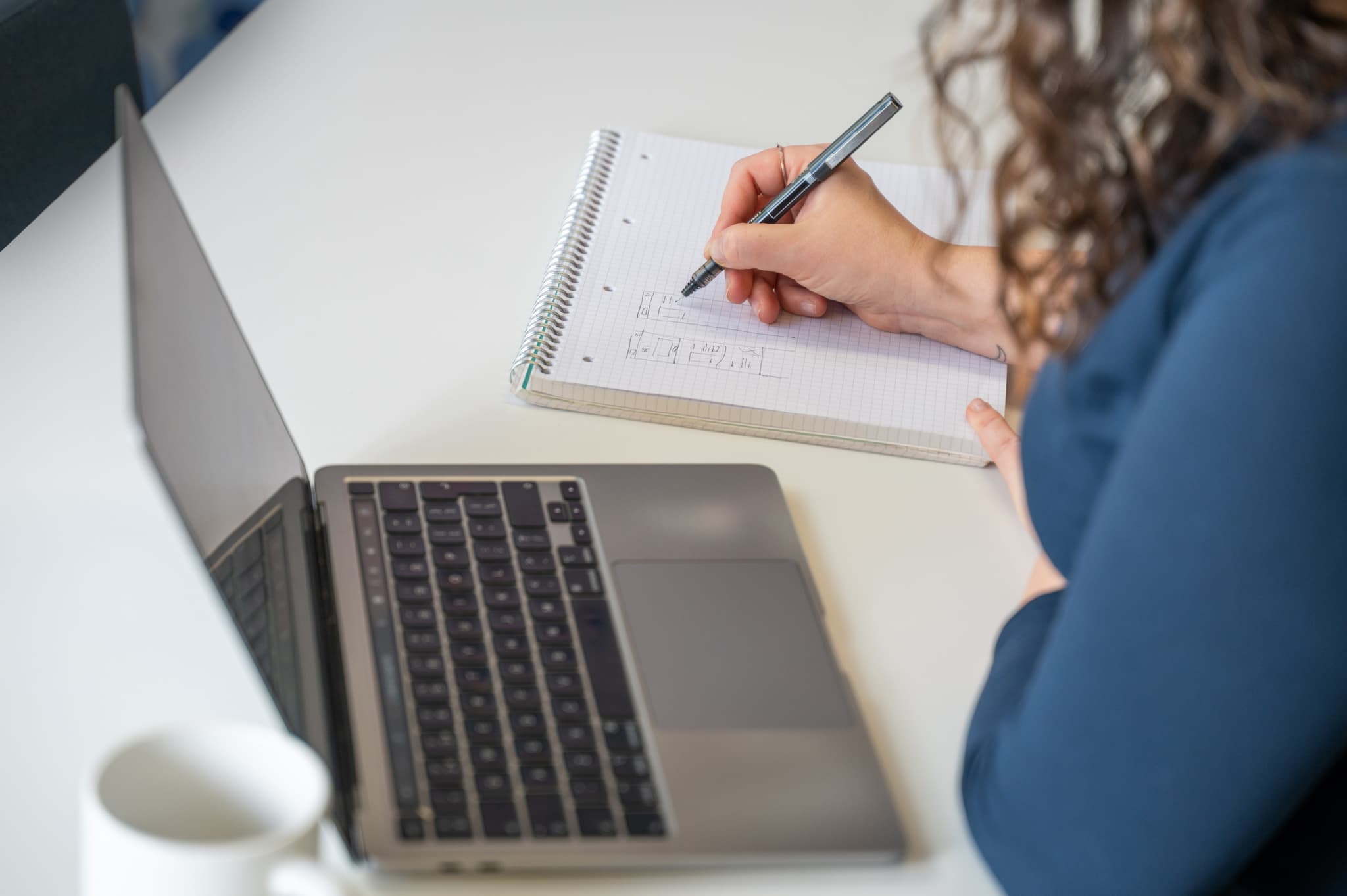 Rachel sitting at a desk with laptop open, sketching some wireframes