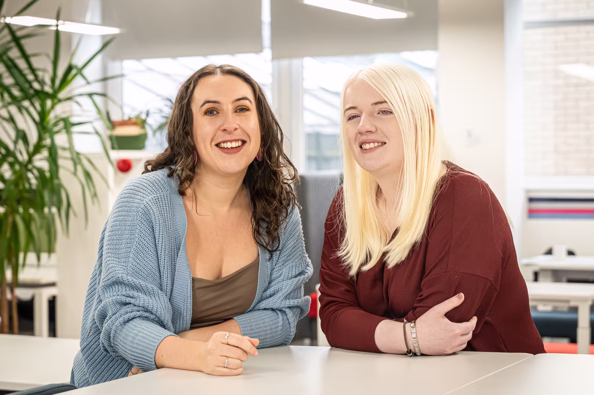 Rachel and her sister sitting next to each other with their arms on the table in front of them. Both women are white, Rachel has dark wavy hair and Hannah has white blonde, poker straight hair. 
