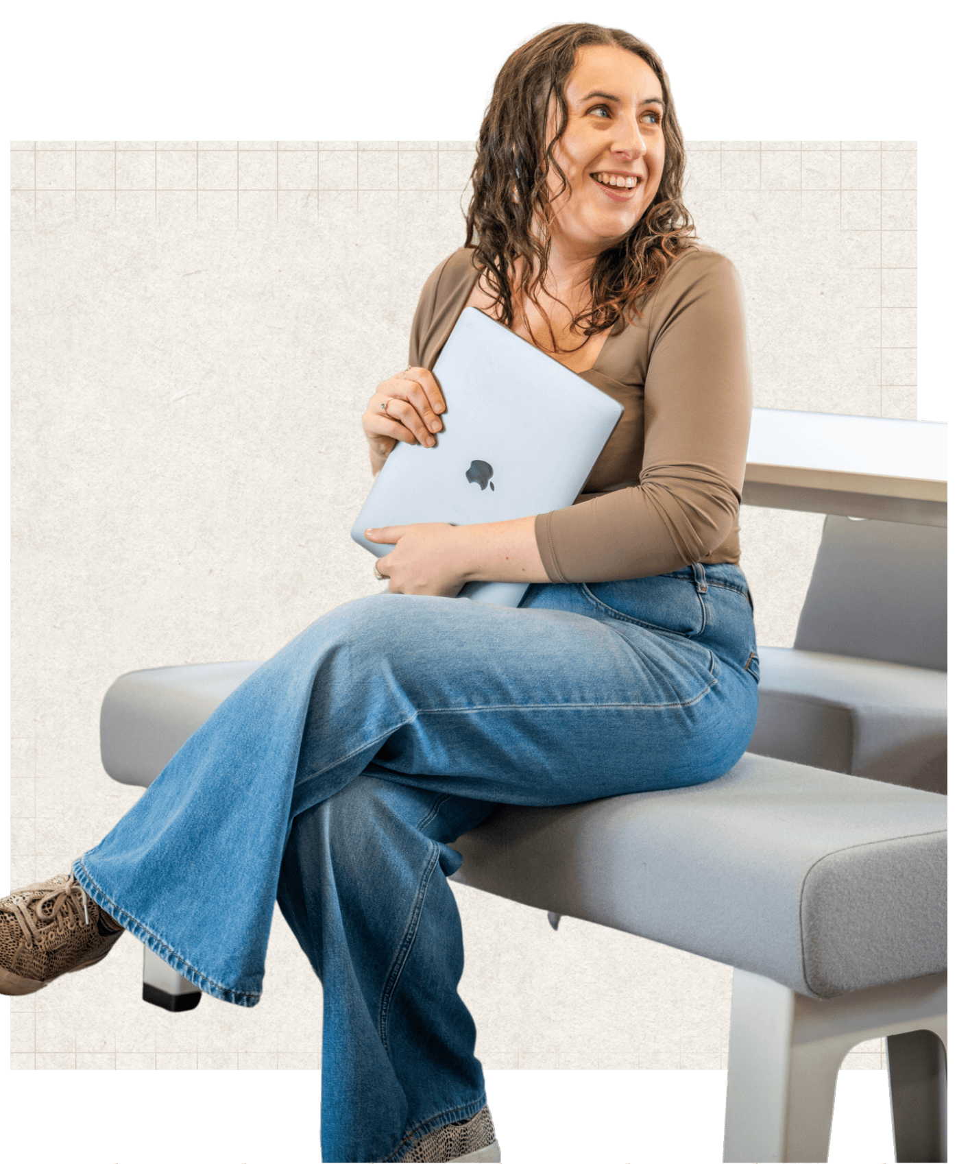 Rachel, a white woman with wavy brown, shoulder length hair sitting holding a laptop, smiling as she looks over to the right of the screen.