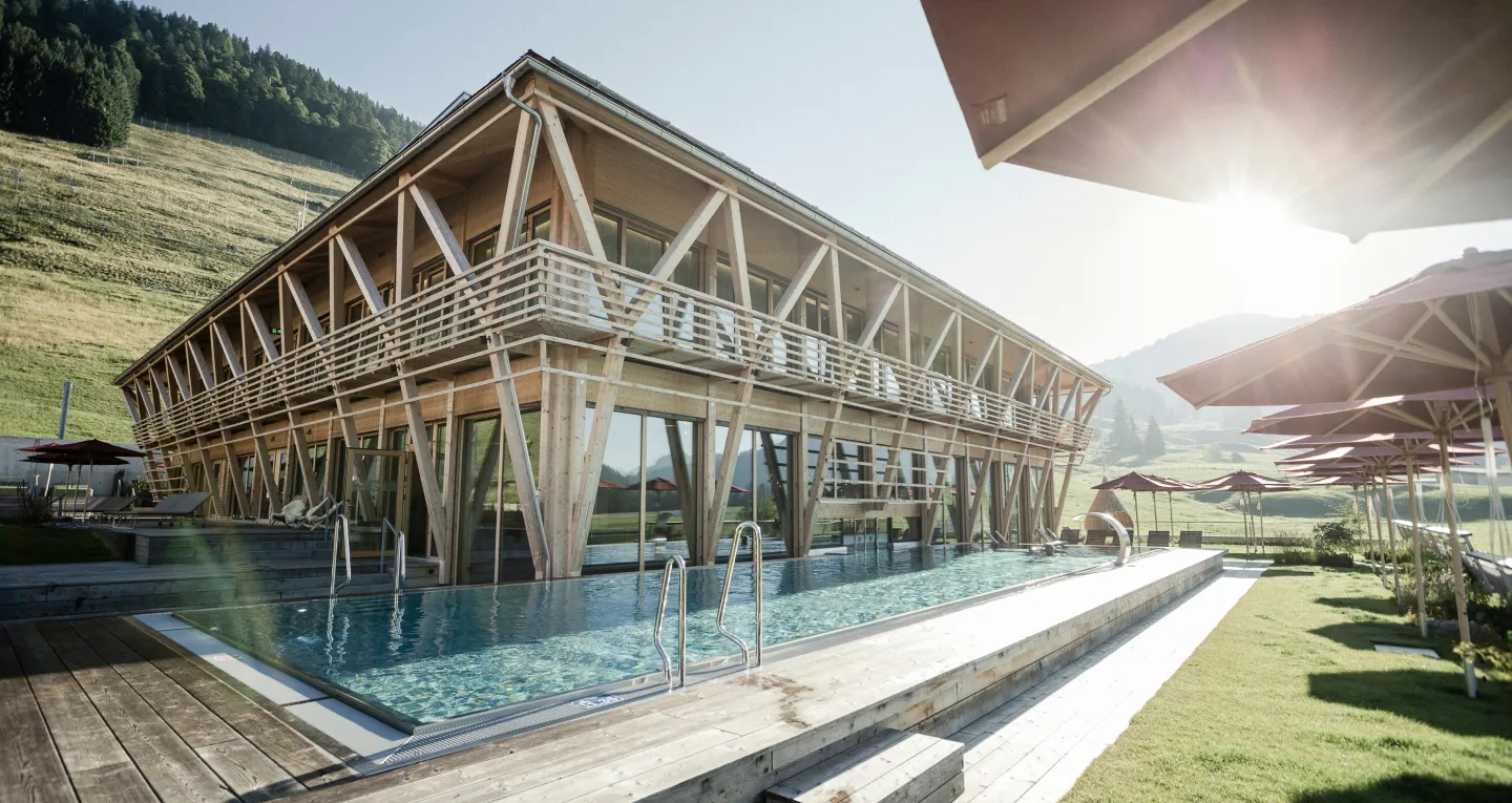 Hotel in Holzbauweise mit Pool in idyllischer Berglandschaft. Caroline Wolf Immobilien