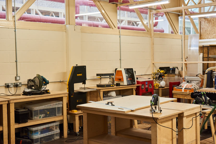 Interior view of a woodworking workshop with workbenches and various power tools like saws and sanders.