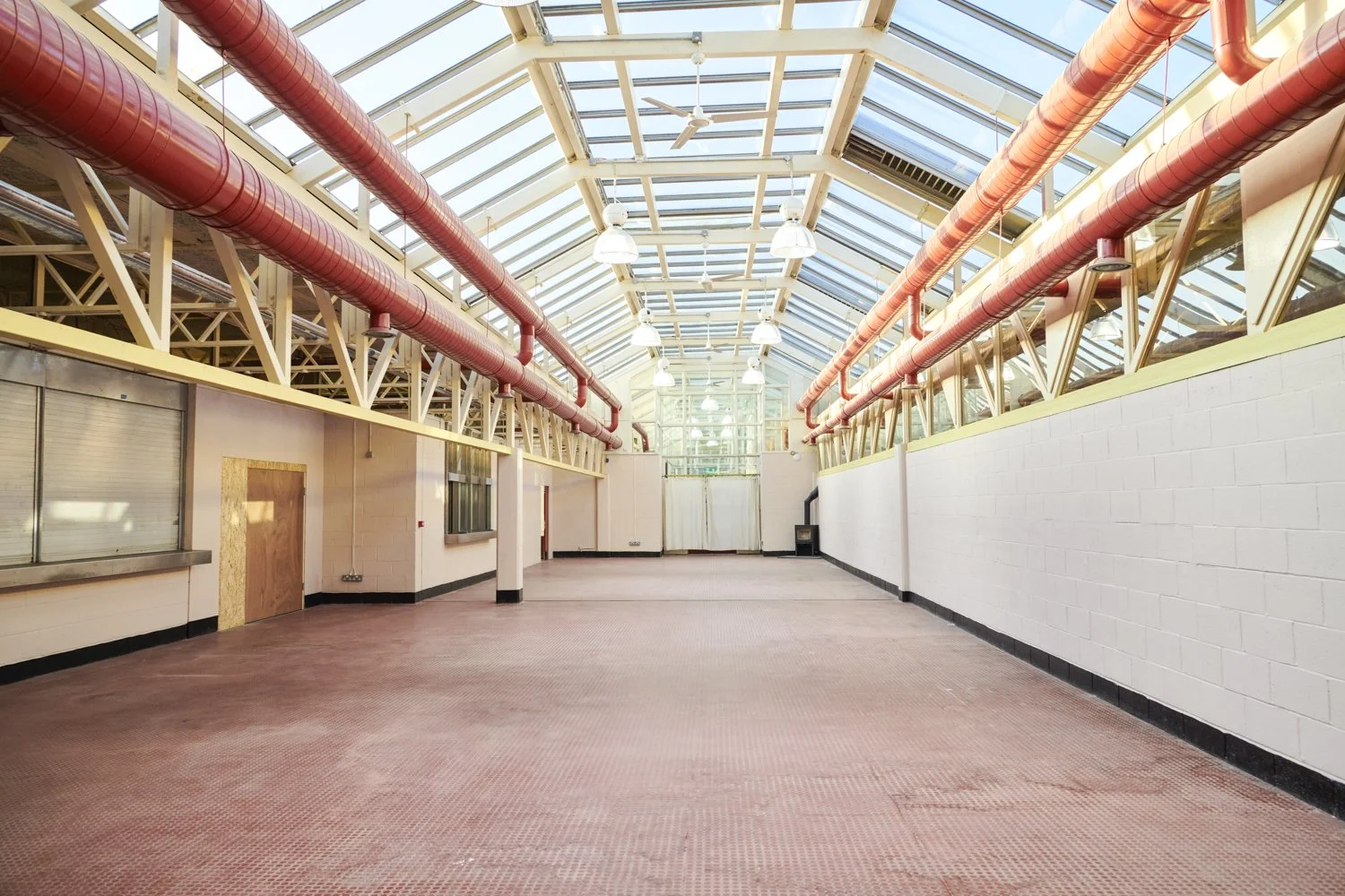 Empty industrial-style room with skylight ceiling, red ventilation pipes, and tiled floor.