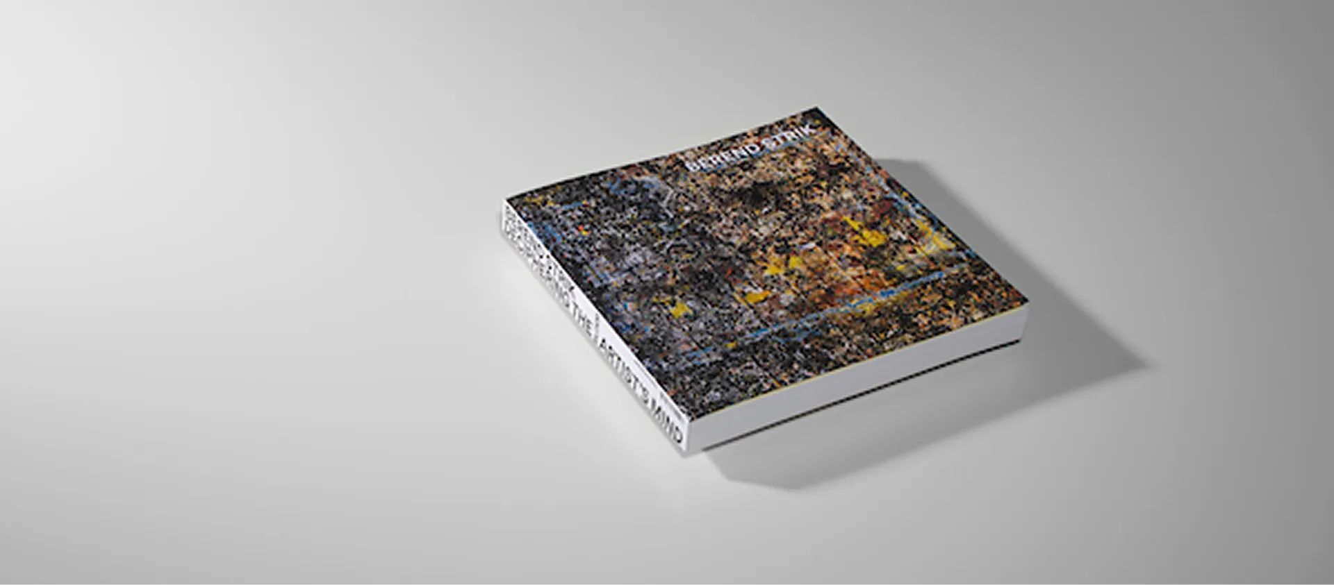 Closed book with an abstract multicolored cover placed on a plain light gray surface.
