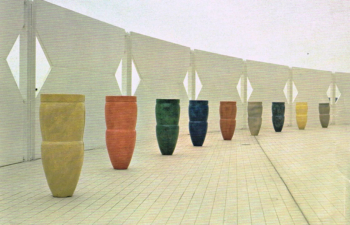 Row of colorful ceramic vases displayed on a tiled floor with white geometric wall panels in the background.