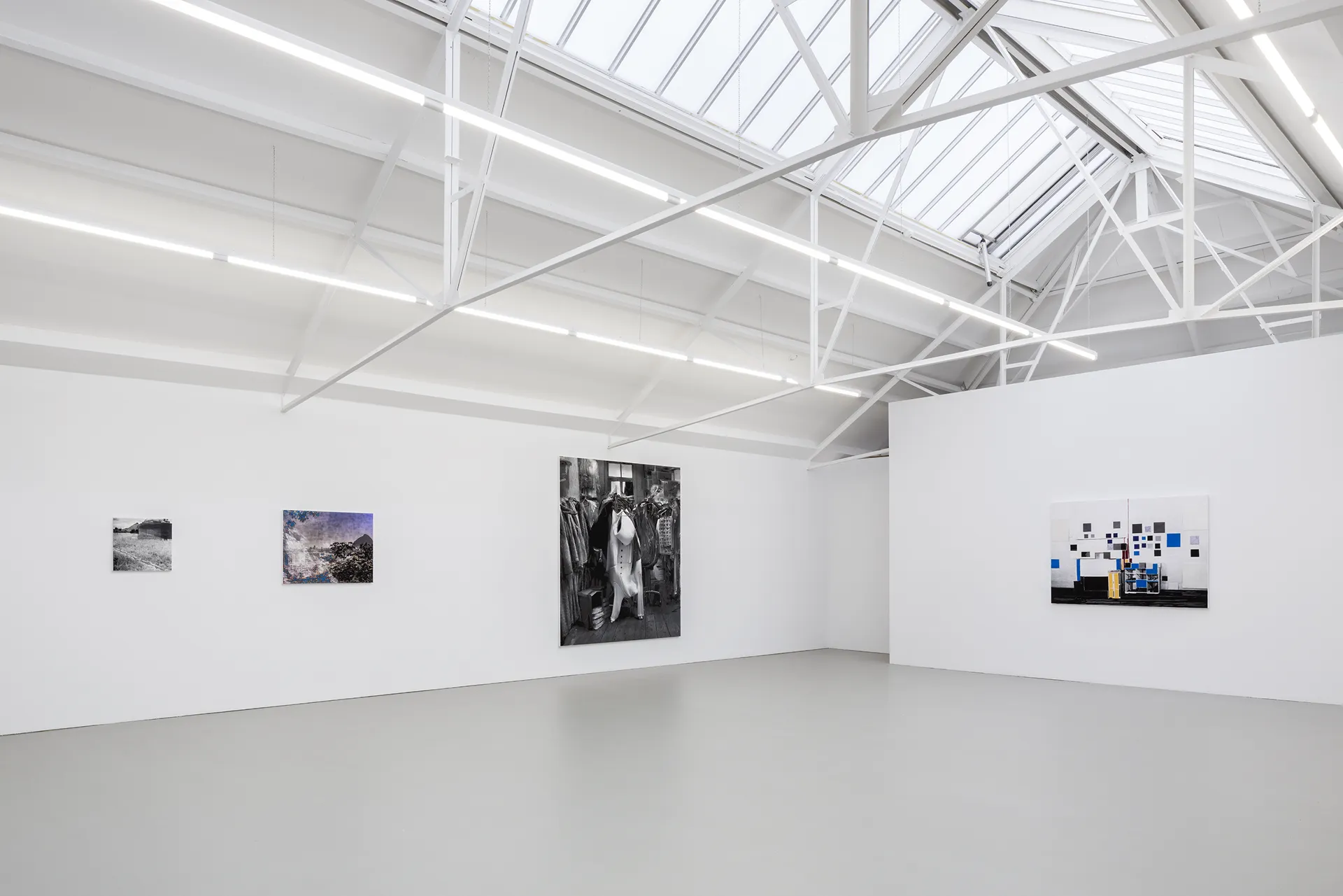 Minimalist white gallery room with four modern artworks hanging on the walls and a skylight ceiling.