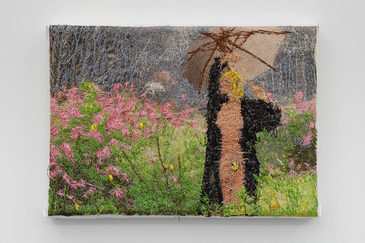 Textile art piece depicting a person with blonde hair holding a brown umbrella standing in a lush garden with pink flowers and green grass.