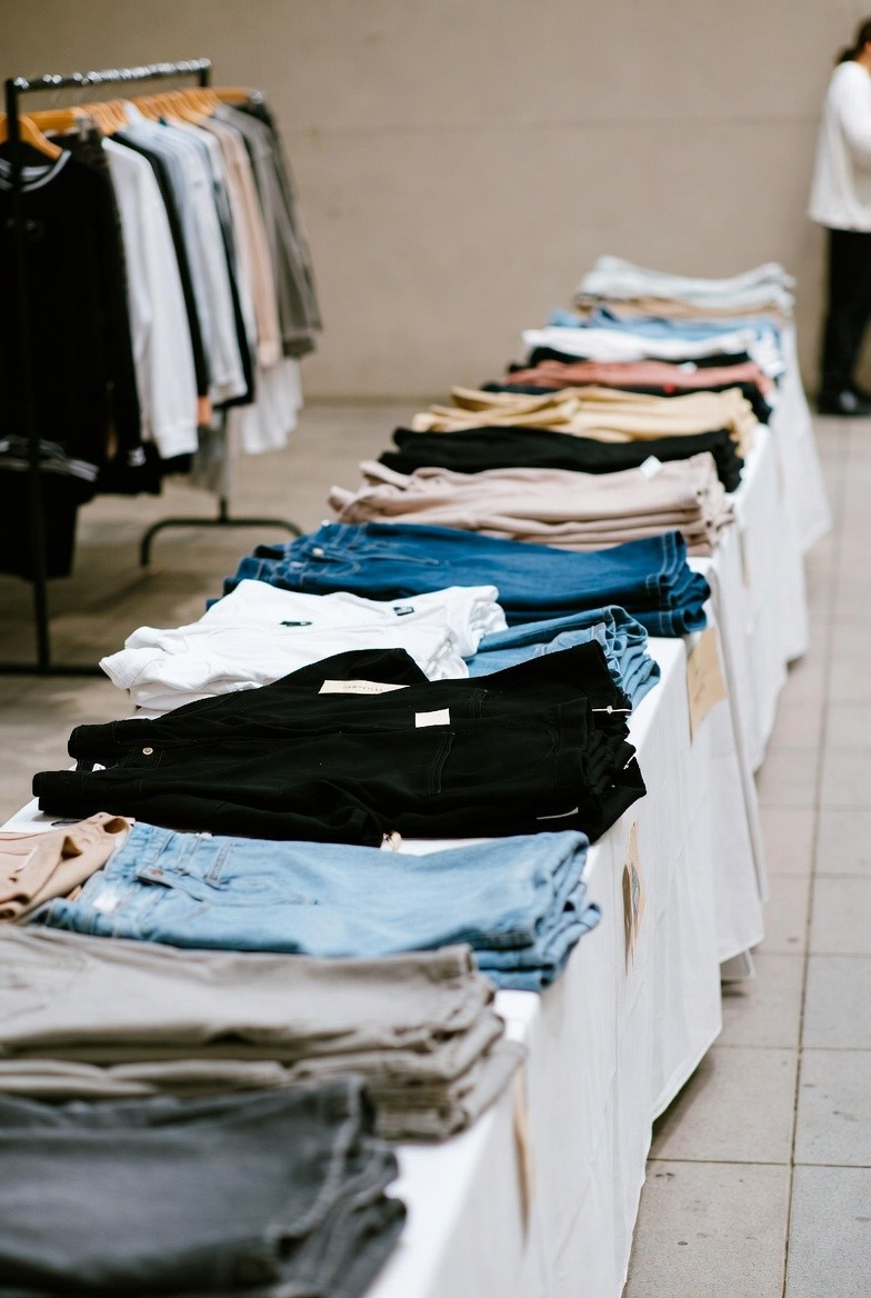 Neatly folded women's high-waisted jeans and denim trousers in various colors – black, white, light blue, dark blue, and beige – displayed on a table in a clothing store.