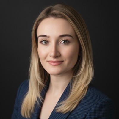 Portrait of a blonde woman wearing a blue textured blazer against a dark background.