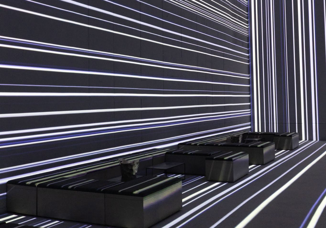 Modern interior with black low sofas arranged against mirrored walls and floor, all featuring white horizontal and vertical glowing light stripes creating a futuristic effect.