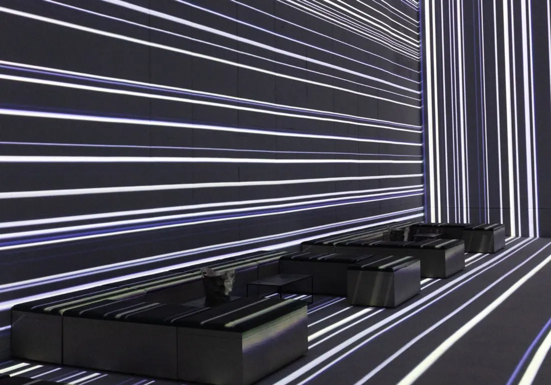 Modern interior with black low sofas arranged against mirrored walls and floor, all featuring white horizontal and vertical glowing light stripes creating a futuristic effect.
