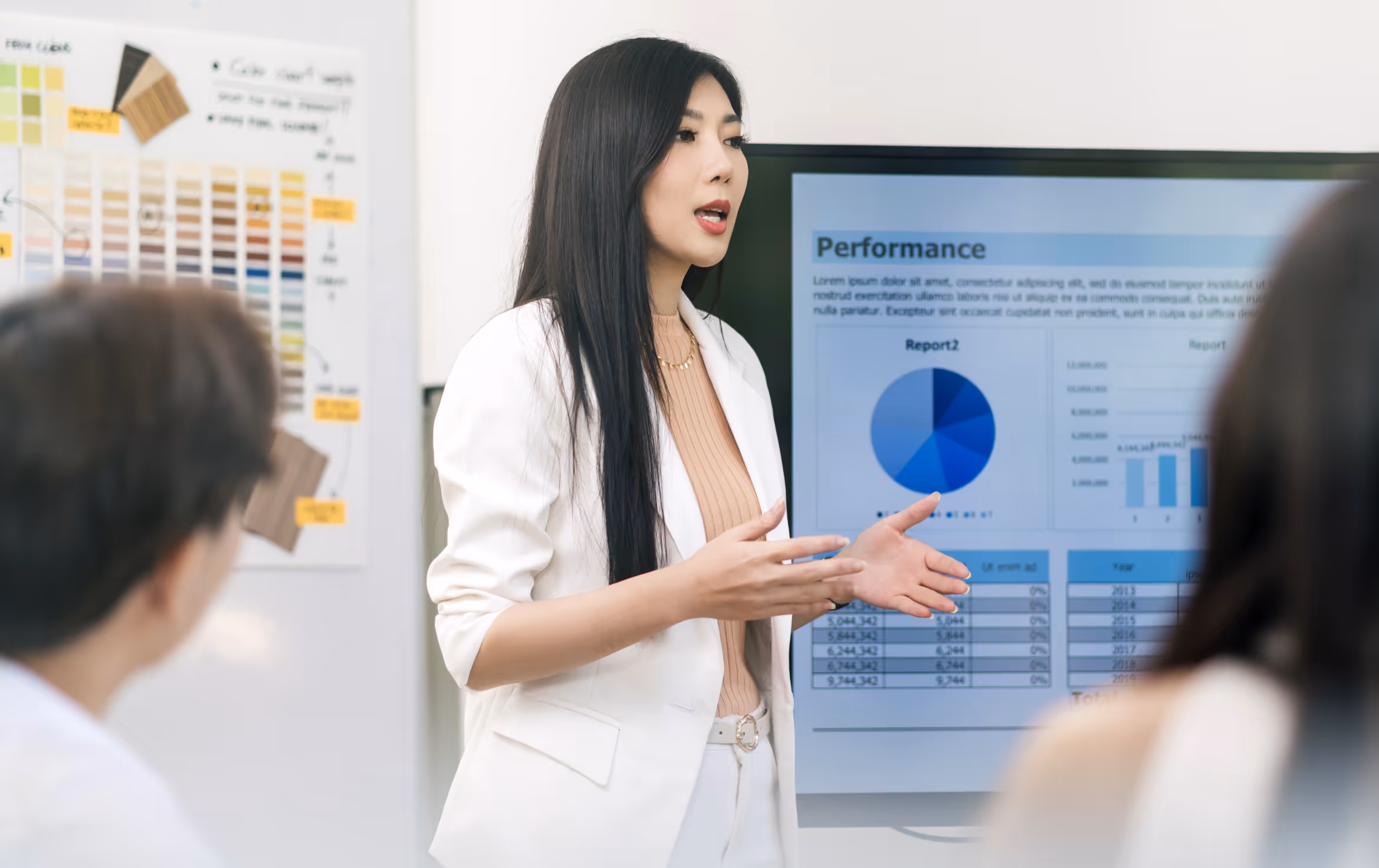 Woman in white blazer giving a presentation with a performance report displayed on a screen behind her.