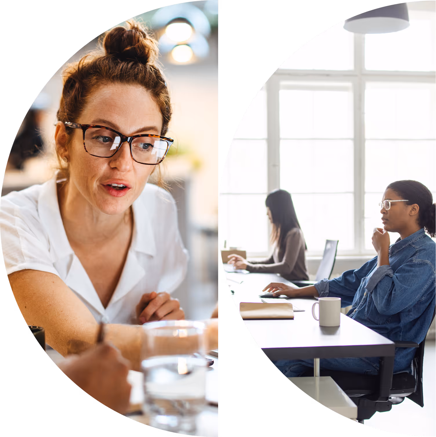 Two women working at desks in a bright office, one in glasses talking and the other focused on a laptop.