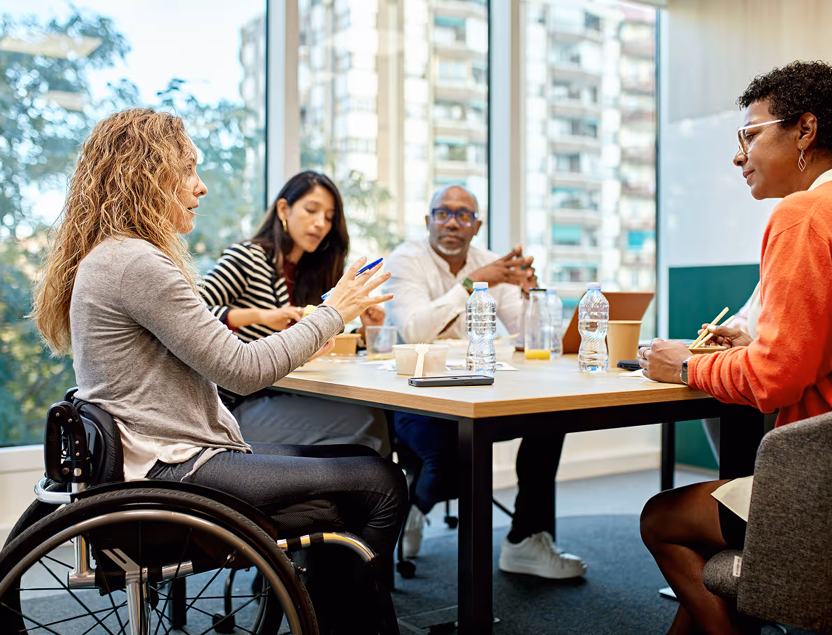 Diverse group of four colleagues having a meeting around a table in a bright office, including a woman in a wheelchair.