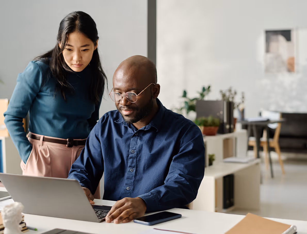 Two colleagues collaborating over a laptop in a bright modern office, with a smartphone on the desk.