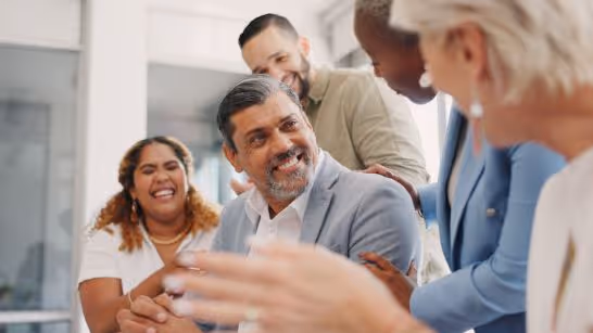 Diverse group of five coworkers smiling and engaging warmly in a bright office.