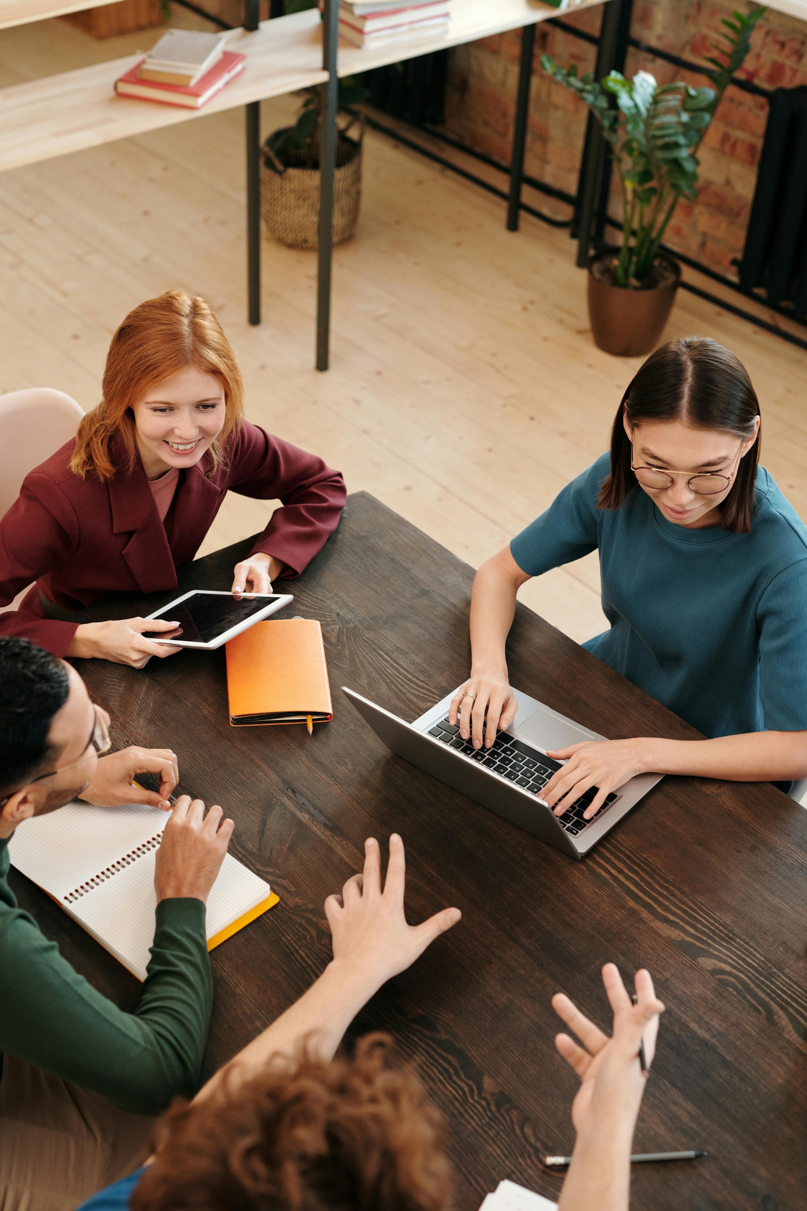 Business team collaborating in an office meeting with laptops, tablets, and notes on a wooden desk.