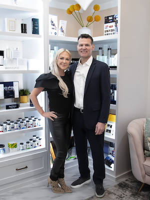 Smiling middle-aged woman with long blonde hair wearing a light blue shirt in a softly lit room.
