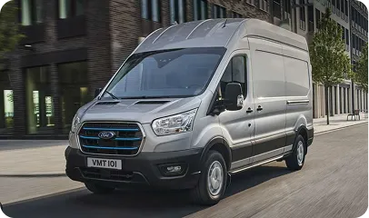Silberner Ford Transit Kleintransporter fährt auf einer Straße vor modernen Gebäuden.